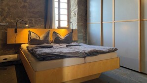 A modern bedroom with a stone wall, a large window with curtains, a bed with a headboard, and a wardrobe. - Ab 1 Person: Rittergut mit Kamin, Fasssauna und mehr Nähe Sächsische Schweiz Dresden (Großharthau)