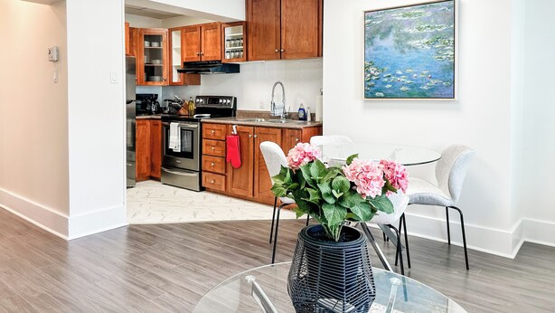 A modern kitchen with wooden cabinets, stainless steel appliances, and a dining area with a glass table and chairs.