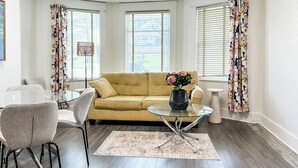 A living room with a yellow sofa, a glass coffee table, and a floral vase.