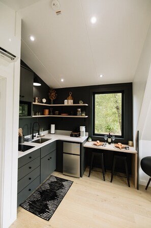 A modern kitchen with a built-in dishwasher, a dining area with a table set for two, and a window with a view of greenery.