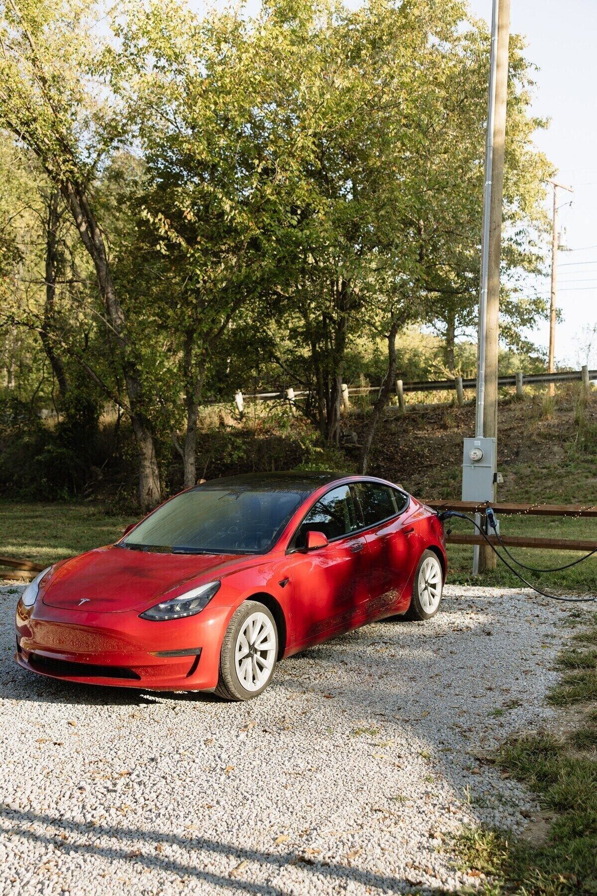 A red car parked on a gravel path with trees in the background.