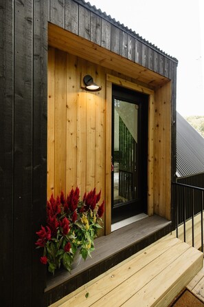 A wooden building with a black door and a small porch with red flowers.