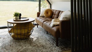 A cozy room with a large window, a leather sofa, a round coffee table, and a small plant.