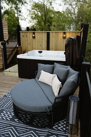 A cozy outdoor seating area with a cushioned lounger, a hot tub, and a patterned rug.
