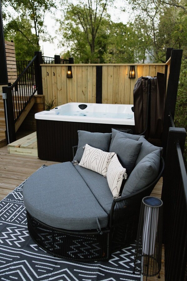 Un espace de détente extérieur accueillant, avec un confortable fauteuil rembourré, un jacuzzi et un tapis à motifs.