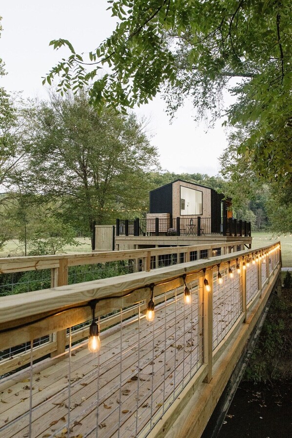 A modern wooden deck with string lights, leading to a contemporary building with large windows and a balcony.