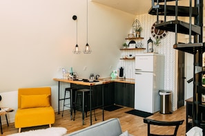 A compact kitchen with a modern design, featuring a white refrigerator, wooden countertops, and hanging pendant lights.