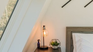 Une chambre avec un plafond en pente, une table de chevet avec une lampe, une petite plante et un panier.