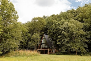 A cabin in a forest with a triangular roof and wooden deck.