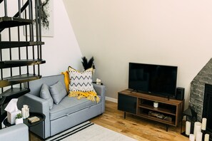 Een moderne woonkamer met een grijze bank, een flatscreen televisie, een houten tv-meubel en een open haard.