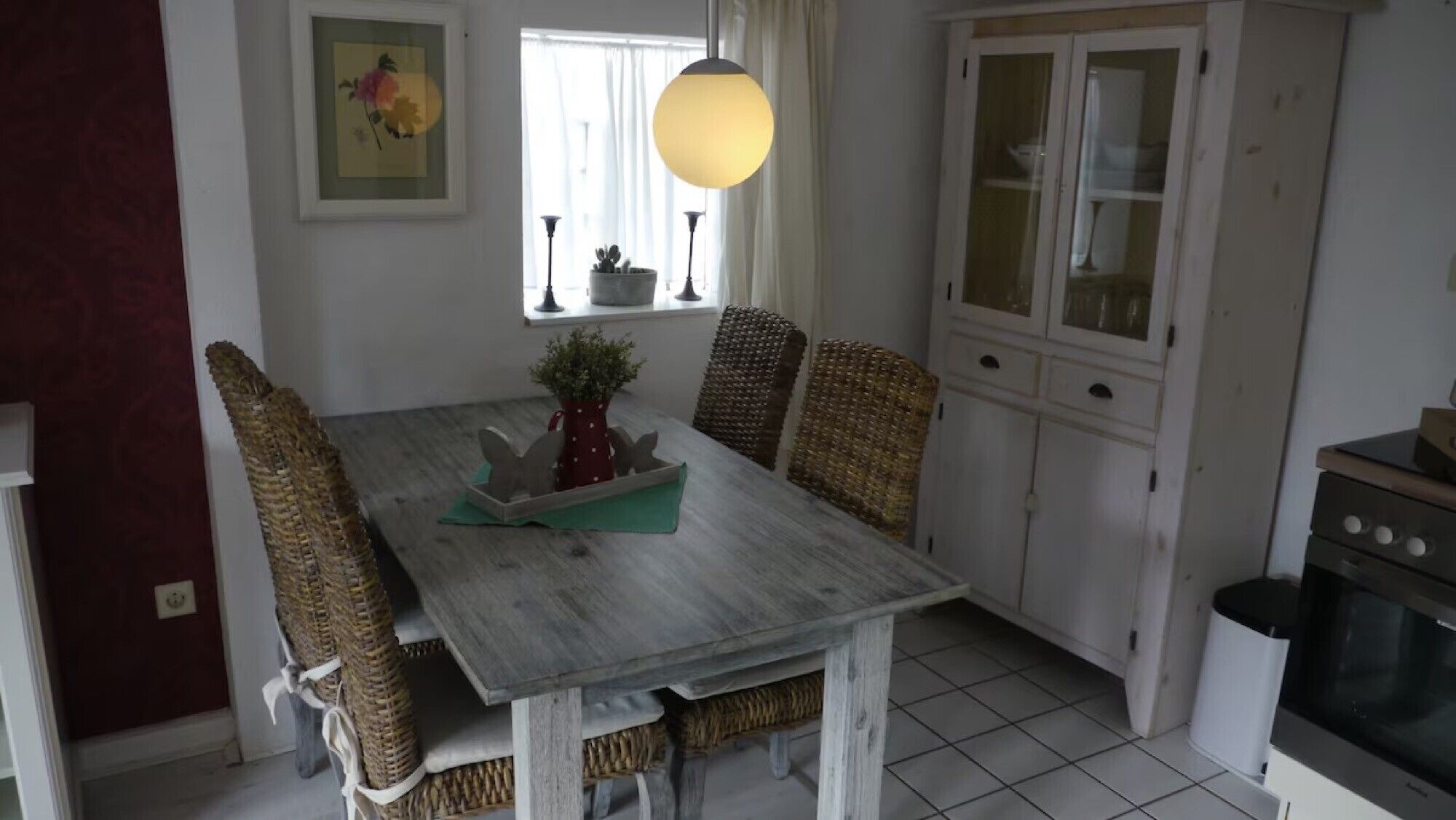 Ein Essbereich mit Holztisch, Korbstühlen, einem Blumentopf und einer Pendelleuchte.