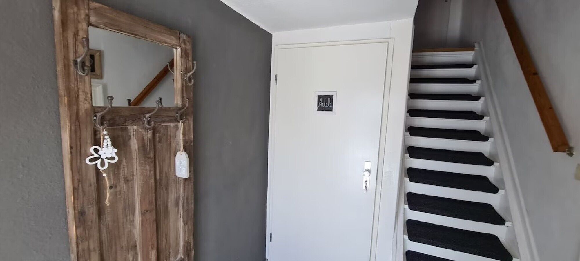 A wooden door with a mirror, a white door with a nameplate, and a staircase with black steps.
