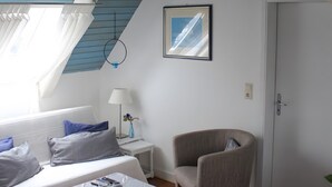 A room with a sloped ceiling, a bed with blue bedding, a small table with a lamp, a chair, and a door. - Holiday Home 'Fachwerkhaus Korntenne' with Mountain View, Private Terrace and Wi-Fi (Willingen (Upland))