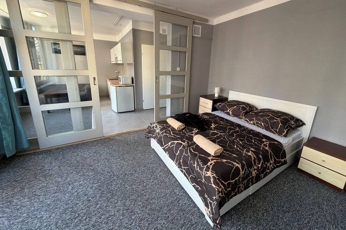A bedroom with a bed, a nightstand, a dresser, a mirror, and a sliding glass door leading to a bathroom.