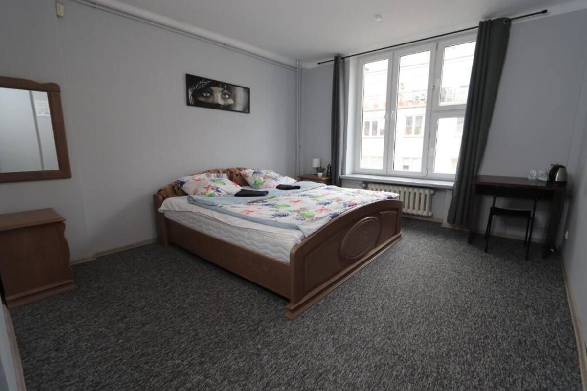 A bedroom with a bed, a desk, a chair, a window, and a radiator.