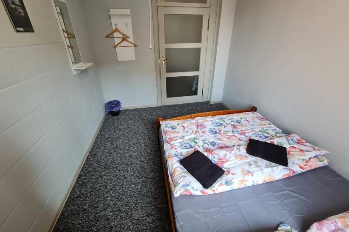 A small, compact room with a single bed, a mirror, a wardrobe, and a door.