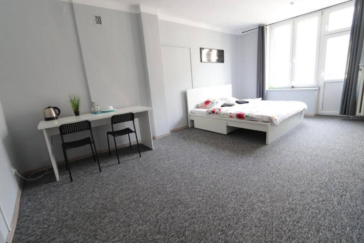 A bedroom with a bed, a desk, two chairs, a small plant, and a window.