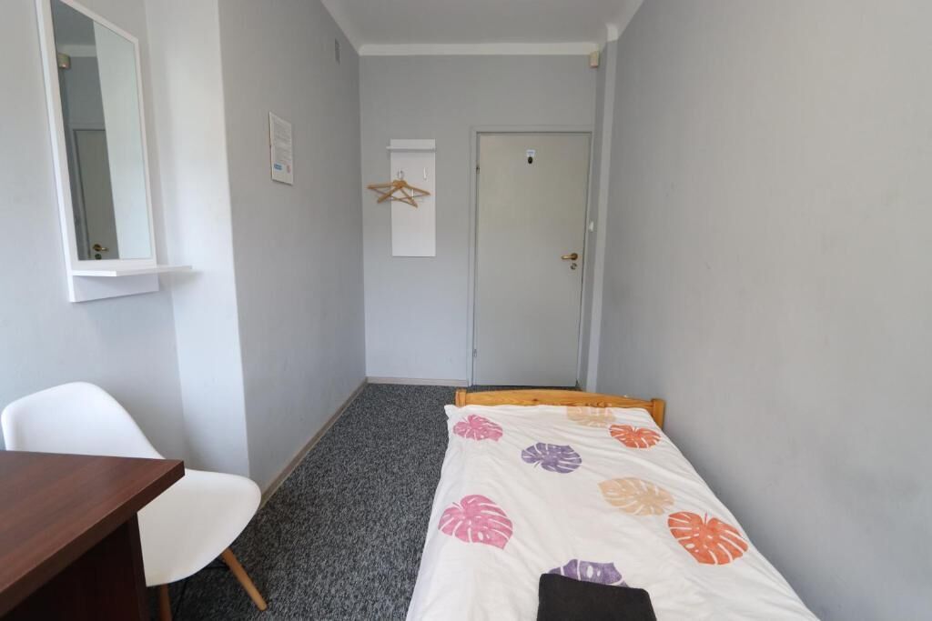 A small, narrow room with a single bed, a desk, and a chair.
