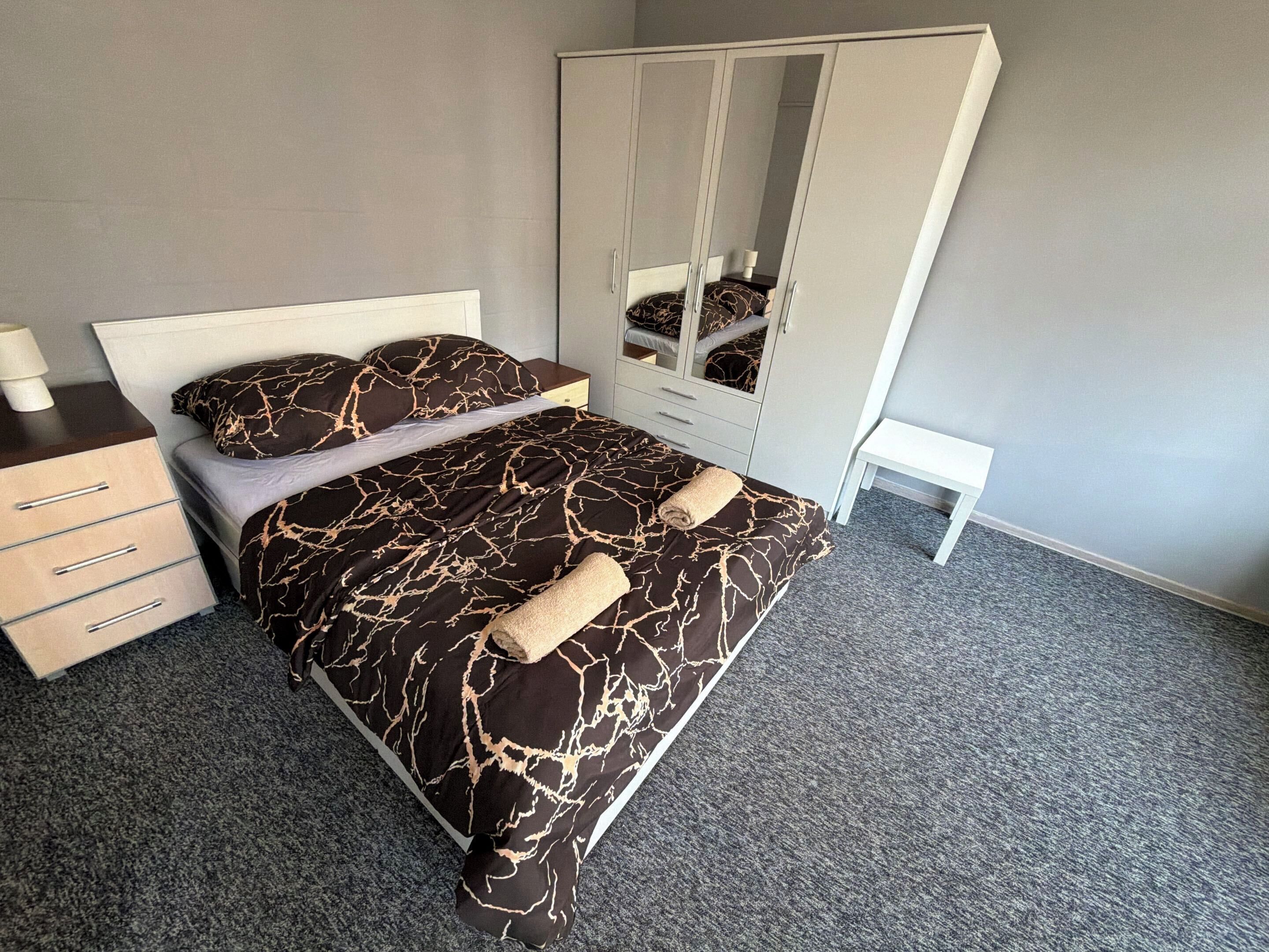 Une chambre à coucher comprenant un lit, une armoire, une table de chevet et un petit tabouret.