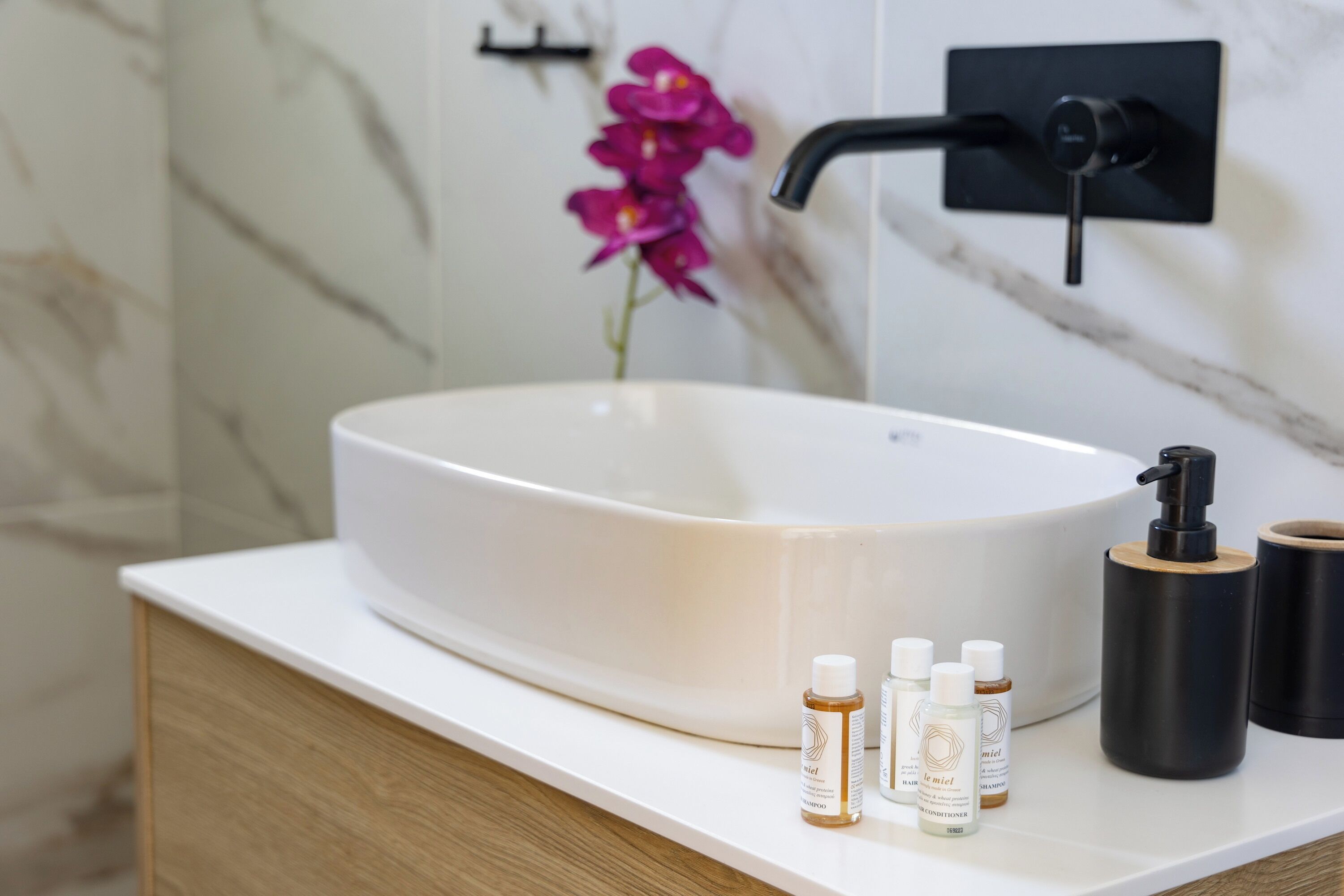 Um banheiro com uma pia grande e branca, um móvel de vaidade de madeira e uma torneira preta. Há três frascos de shampoo e condicionador sobre o móvel.