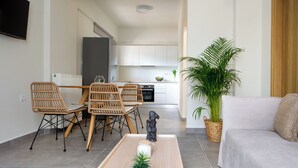 A modern living room with a sofa, a dining table with chairs, a small statue, and a potted plant. - Sueno Studios and Apartments (Chania)