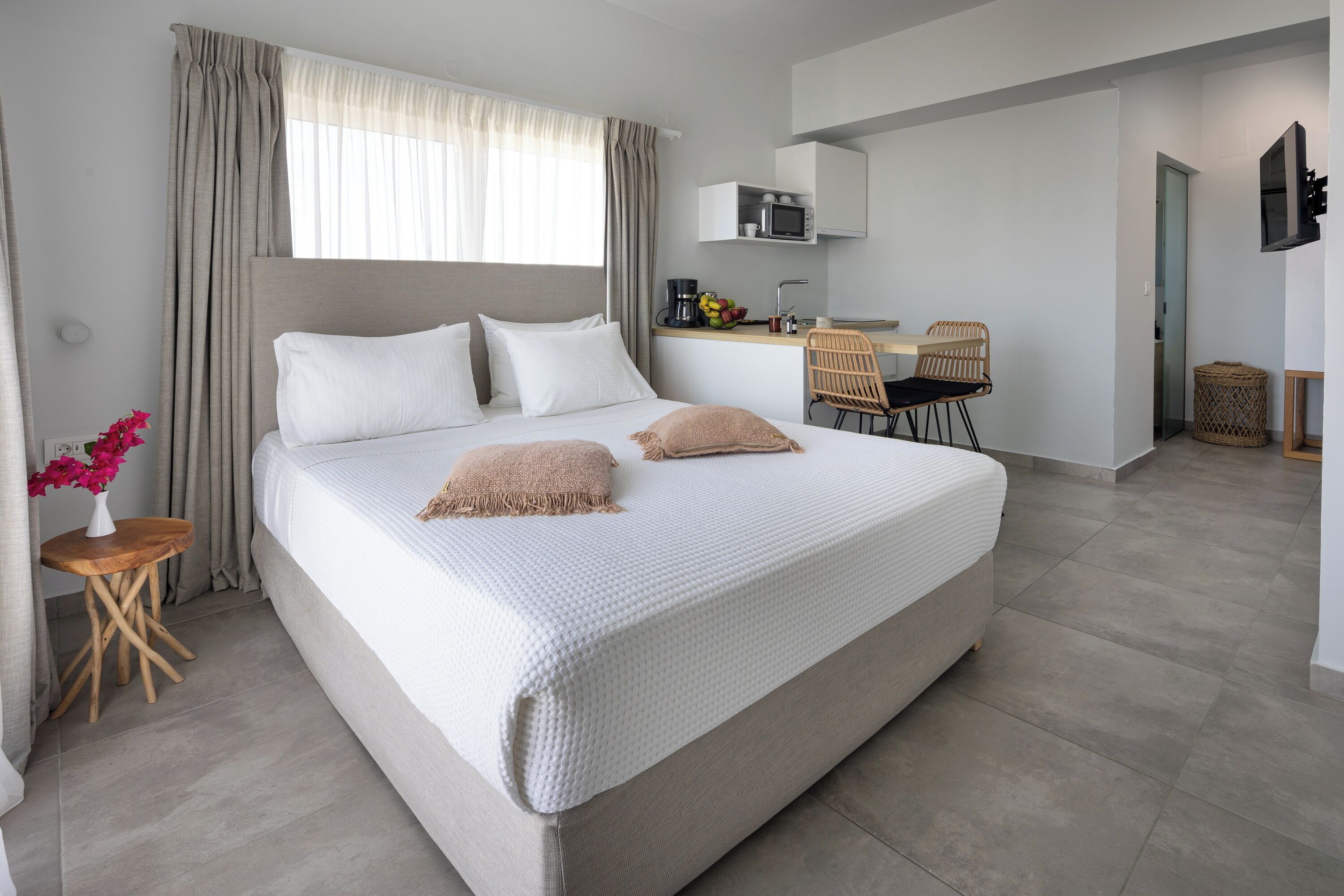 A modern hotel room with a large bed, a small desk, a chair, and a TV.