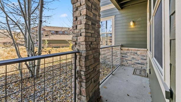 A balcony with a stone pillar, metal railing, and a view of a residential area.