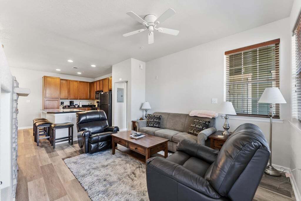 Una sala moderna con un sofá, sillones, una mesa de centro y un comedor con armarios de madera y un refrigerador.