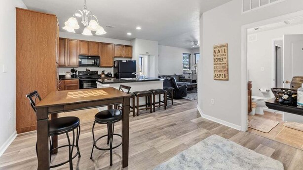 A modern kitchen with wooden cabinets, a central island, and a dining area with a chessboard. - Ten Mile B-102 Ground floor 2 bedroom with private patio upscale modern interior (Granby)