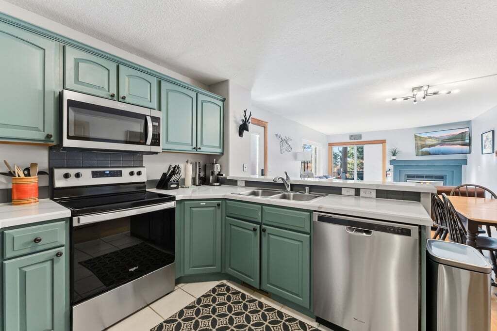 A modern kitchen with teal cabinets, stainless steel appliances, and a patterned rug.