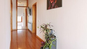 A hallway with wooden flooring, a potted plant, a framed artwork on the wall, and a door at the end.
