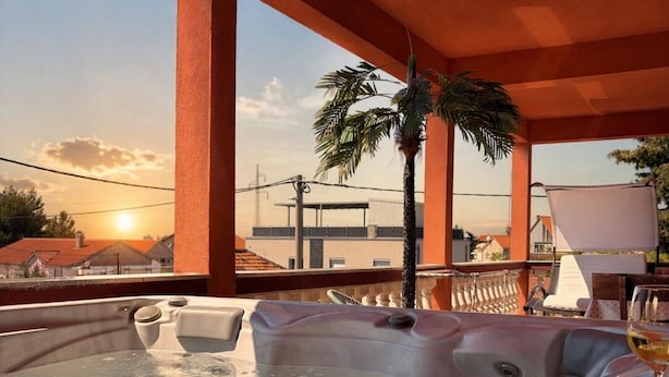 A hot tub with a sunset view, a palm tree, and a glass of wine on a table.