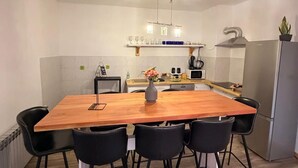 A modern kitchen with a wooden dining table, black chairs, a built-in oven, and a stainless steel refrigerator.