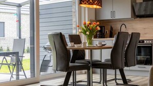 A modern kitchen with a dining area, featuring a table with chairs, a vase of tulips, and a pendant light. - Ferienwohnung am See in Harkebrügge mit Sauna, WLAN, Terrasse & Weber-Gasgrill (Barßel)