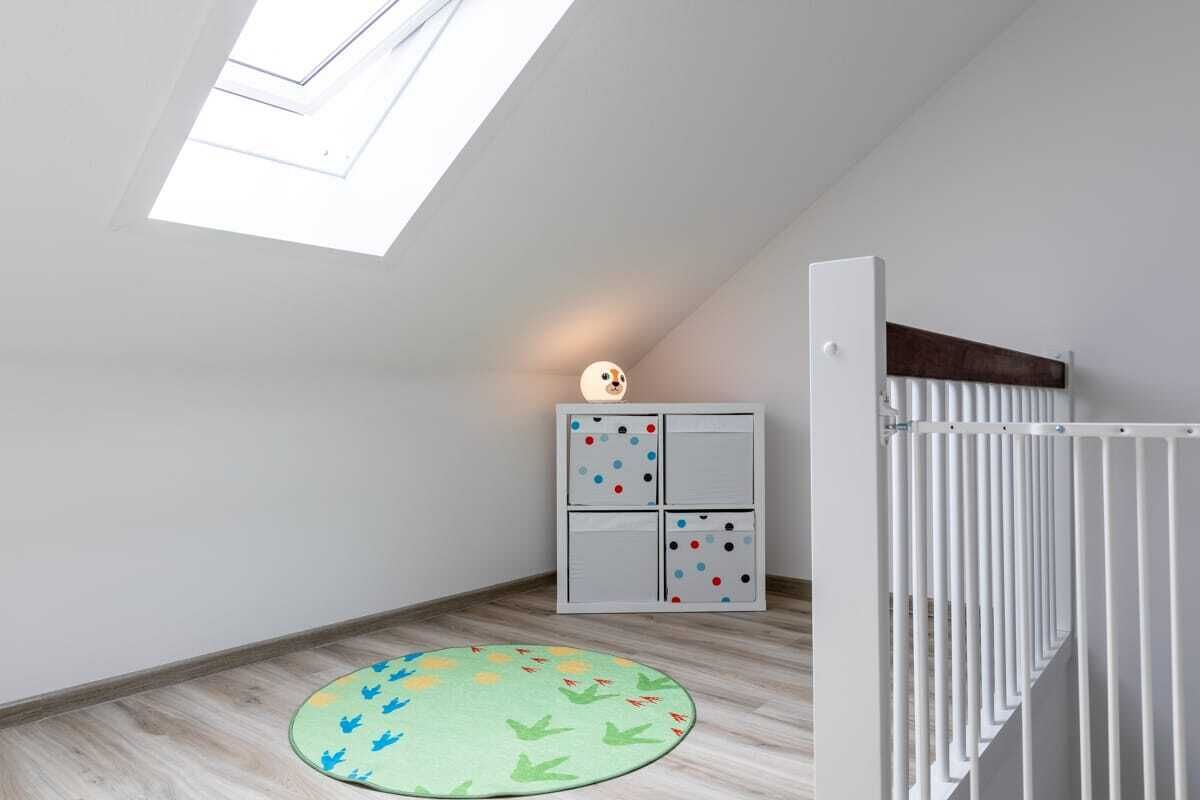 Un espace de jeux pour enfants avec un tapis, un meuble de rangement et une rambarde blanche.