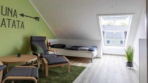 A modern loft bedroom with a sloped ceiling, a bed with a view through a skylight, a green wall with a black arrow, and a small table with chairs. - Ferienwohnung am See in Harkebrügge mit Sauna, WLAN, Terrasse & Weber-Gasgrill (Barßel)