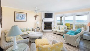 A living room with wicker furniture, a fireplace, a ceiling fan, and large windows. - Oceanfront Private Beach Access & Community Pool! (Southern Shores)