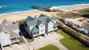 A beachfront property with a pier, a large house with a balcony, and a beach in the background. - Oceanfront Private Beach Access & Community Pool! (Southern Shores)