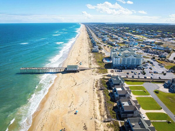 An aerial view of a coastal town with a beach, a pier, and residential buildings.