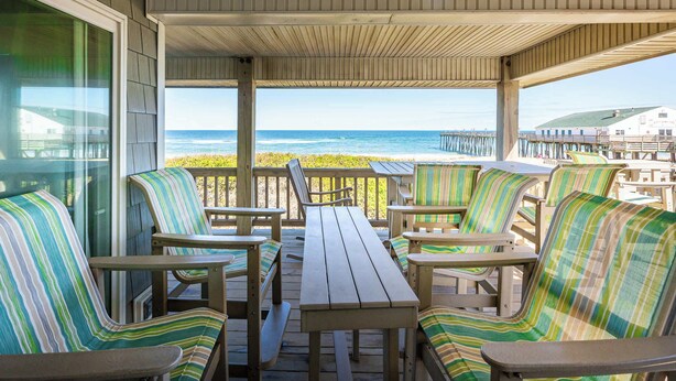 A covered outdoor seating area with wooden tables and striped chairs, overlooking the ocean. - Oceanfront Private Beach Access & Community Pool! (Southern Shores)