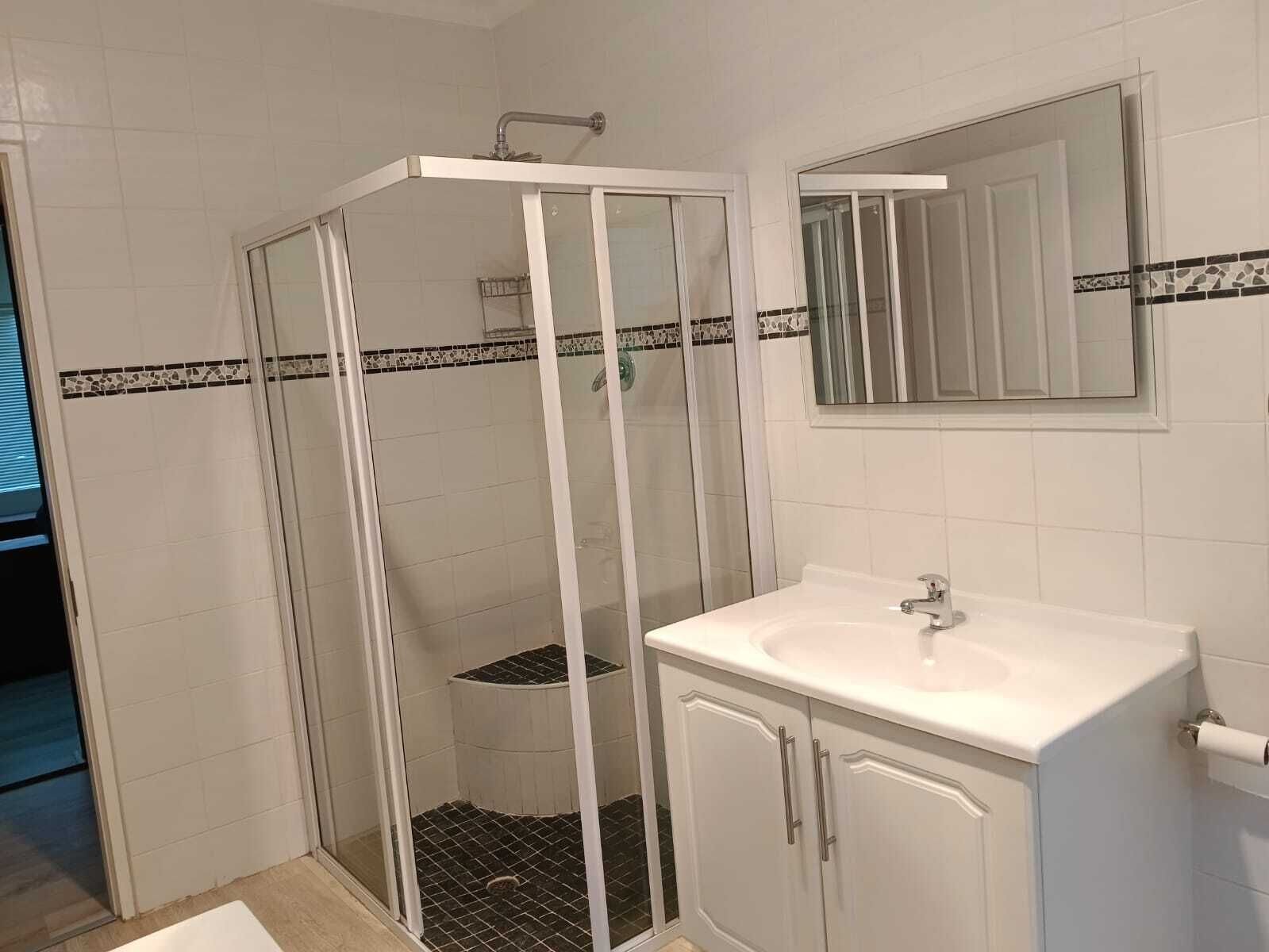Un baño con ducha de vidrio, un lavabo blanco y un espejo encima.