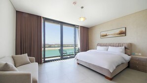A hotel room with a bed, a sofa, a dining table, and a view of the sea. - Silk Valley-4B with Private Beach Access (Al Hamriya)