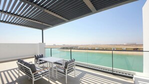 A balcony with a glass railing overlooking a pool and distant cityscape. - Silk Valley-4B with Private Beach Access (Al Hamriya)