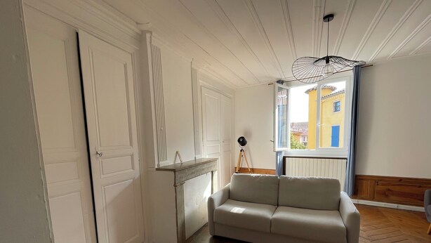 A room with a herringbone wooden floor, a white sofa, a small white table, and a tripod lamp. - Welcome to this large, elegant apartment. (Brioude)