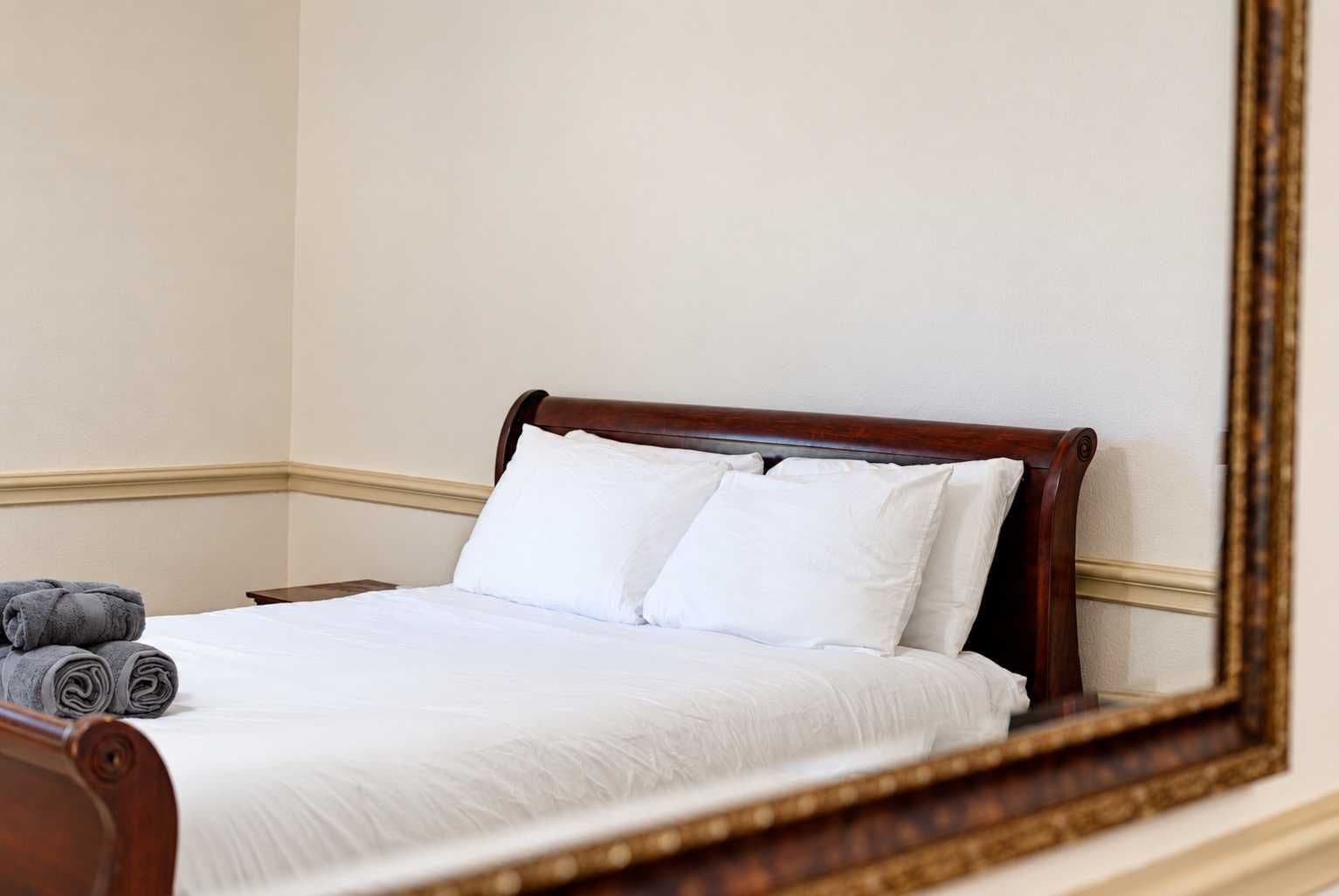A neatly made bed with white linens and two pillows, a wooden headboard, and a rolled-up towel on the side.