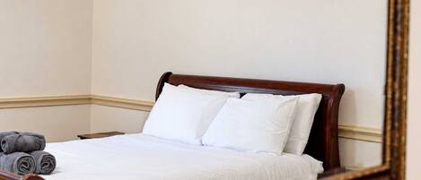 A neatly made bed with white linens and two pillows, a wooden headboard, and a rolled-up towel on the side.