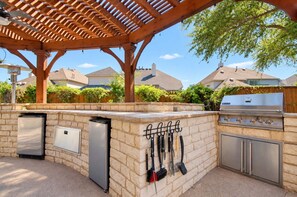 An outdoor kitchen area with a built-in grill, a refrigerator, and various utensils hanging on the wall.