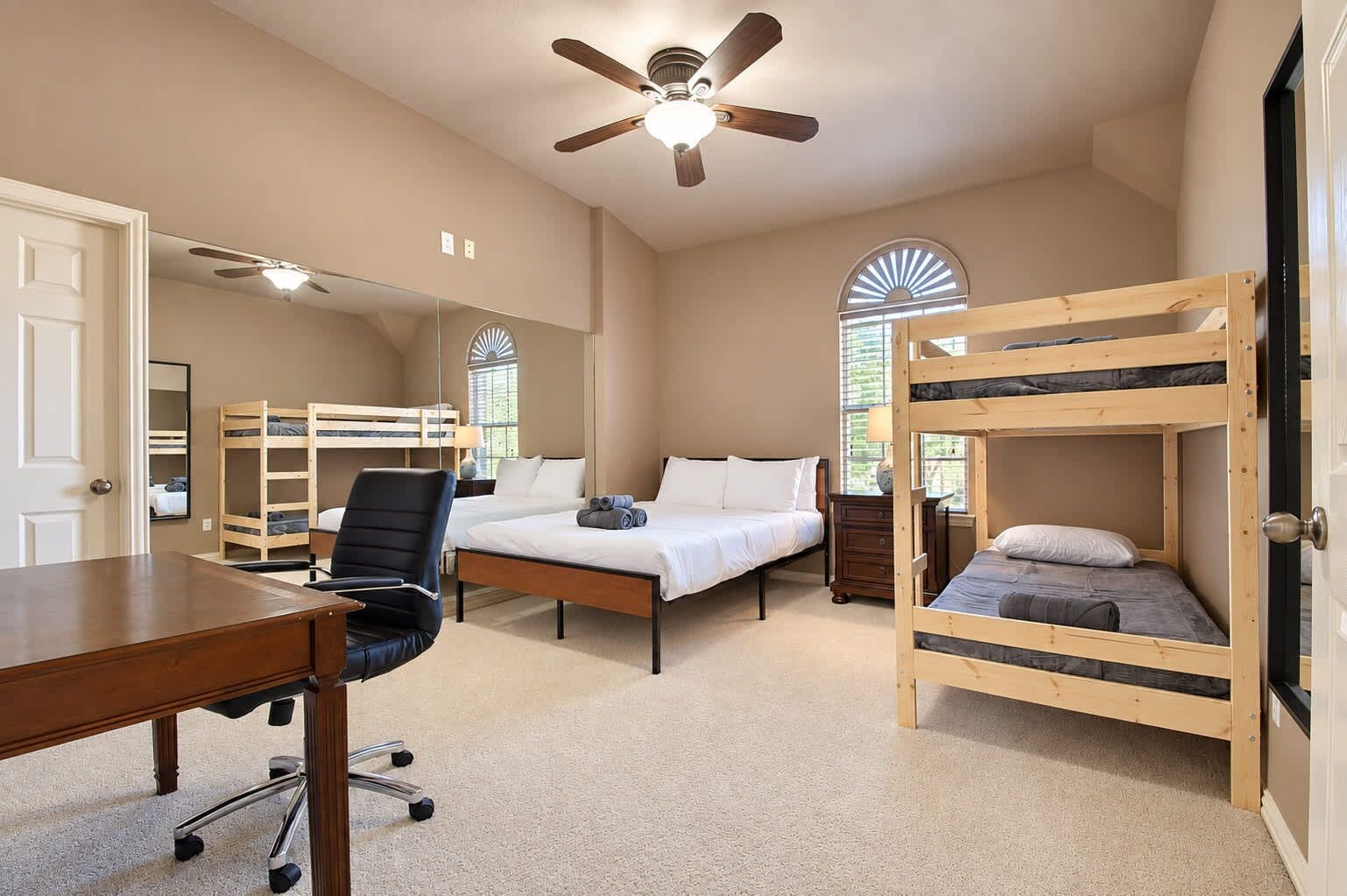 A bedroom with bunk beds, a desk, a chair, a ceiling fan, and a window with a view.