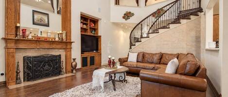 A spacious living room with a fireplace, a leather sofa, a coffee table, and a staircase.