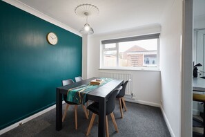 A dining area with a table, chairs, a clock, and a window with a view of buildings outside.